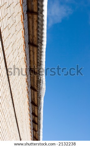 Snow covered roof with icicles, deep blue sky at background