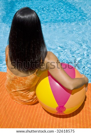 Woman with Long Black Hair Sitting by the Swimming Pool Holding a Beach Ball