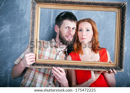 Young loving couple looking through photo frame making an imaginary family portrait