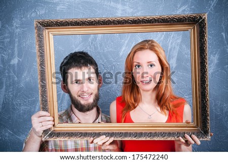 Young loving couple looking through photo frame making an imaginary funny family portrait