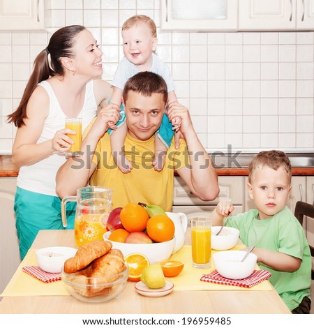 Young happy family with two small kids having breakfast in kitchen
