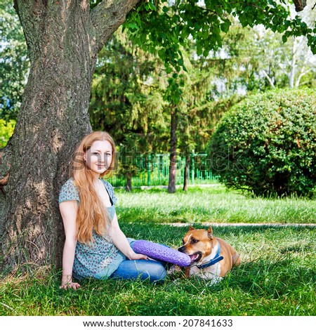 Attractive girl and her dog sitting under tree in park