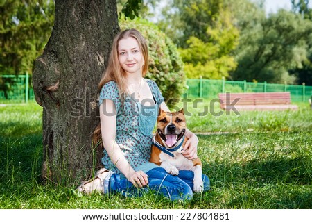 Beautiful girl and her dog sitting under tree in park