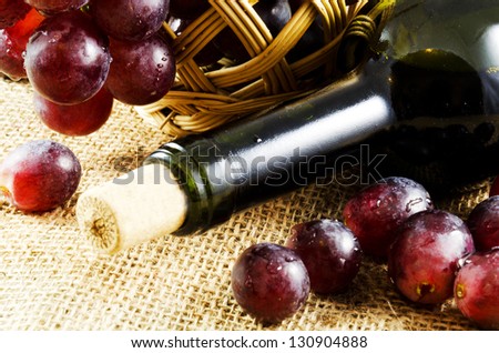 A glass of red wine and grapes in a basket on a jute texture