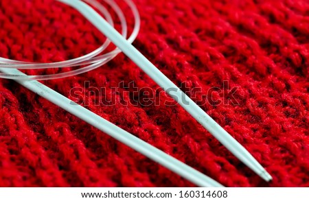 Circular knitting needles on a red wool material.
