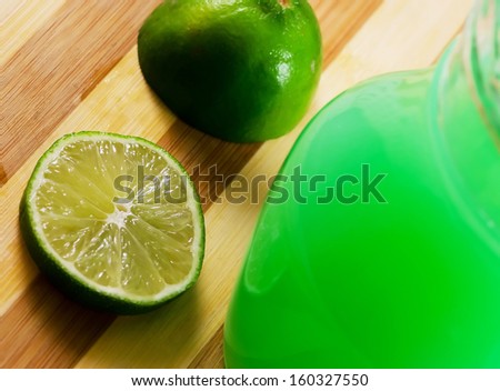 Lime slice and a glass of lime juice on a wooden board.