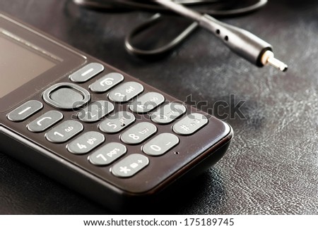Old model of cell phone with accesories on black leather background.