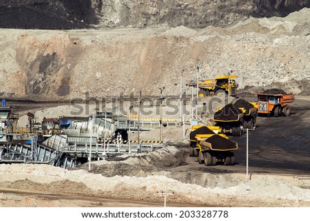 heavy construction tipper trucks dump coal to the conveyor at the lignite opencast mining