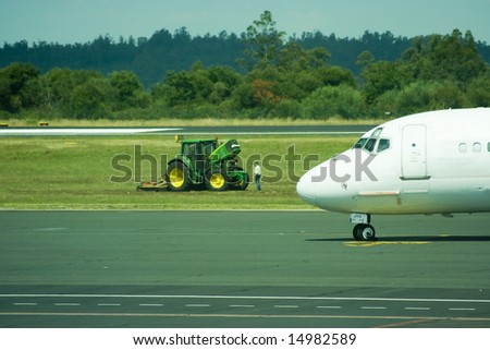White Plane landing in an airport near a tractor with maintenance personnel