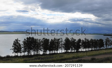 Steppe lake Shira evening view. Dark cumulus clouds reflecting on the still water surface, trees on the shoreline. Natural landscape, Khakassia, Siberia, Russia. July 17, 2014.