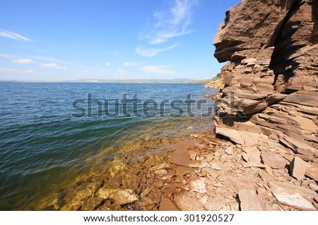 River Yenisei  shore, steep rocky slope above clear water surface. Krasnoyarsk reservoir near village Anash (Novoselovo area, Krasnoyarski krai, Siberia, Russia). Sunny summer day, July 25, 2015.