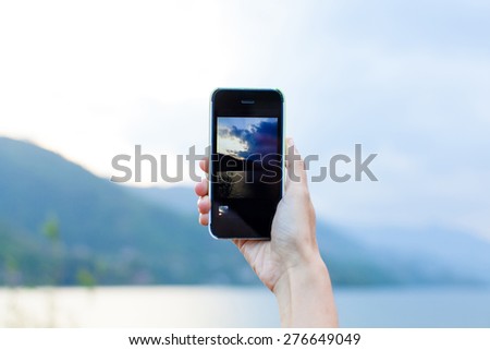 Hand taking photo of the lake and mountain landscape by smartphone
