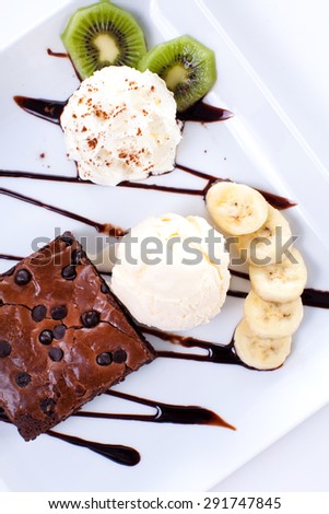Brownie and ice cream with whipping cream and banana slices on plate