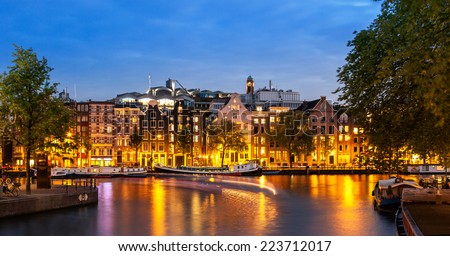 Tail lights of boats crossing canals of Amsterdam at dusk time and apartments illuminated by street lights.