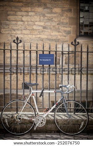 Bicycle tied to a fence e displaying NO Bicycle sign in Oxford, UK.