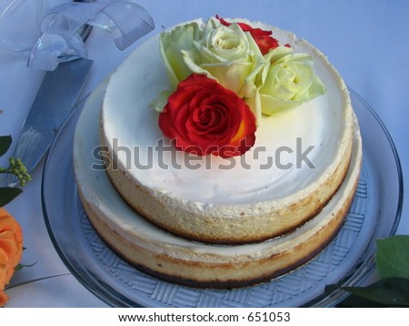 Wedding cake with roses on top set outside for a garden wedding with a slicing knife with bow on handle