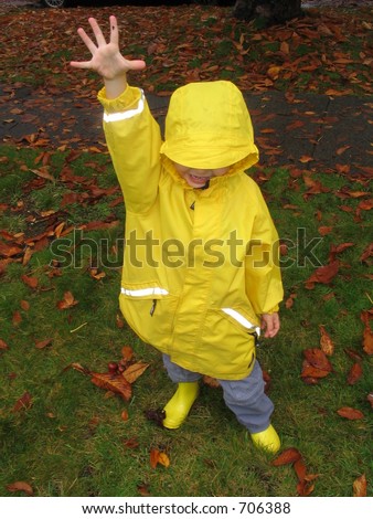 Boy in yellow raincoat and boots holding his hand up with five fingers spread in rain indicating number five