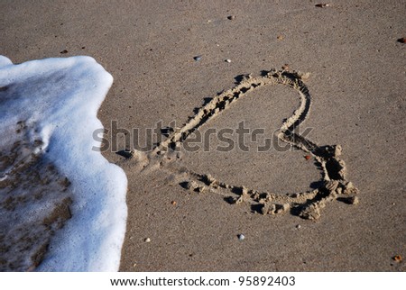 heart painted in the sand is taken away from the tide