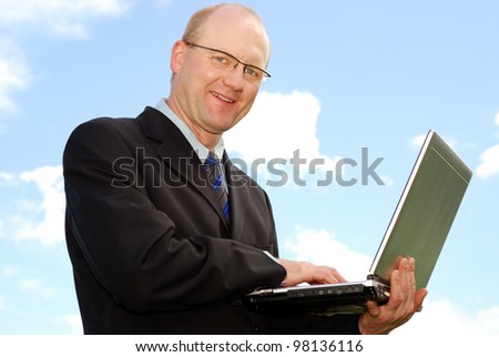 smiling businessman with laptop in front of blue sky