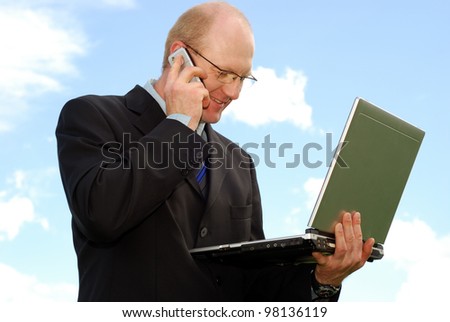 smiling businessman with laptop in front of blue sky