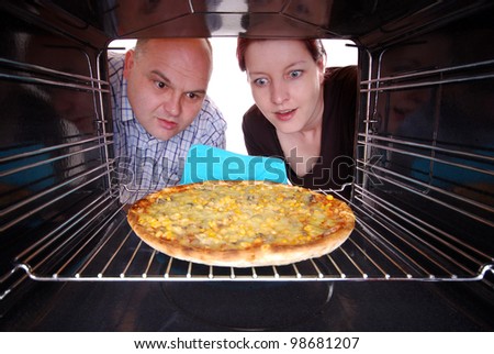 man and woman looks in a oven to their baking pizza