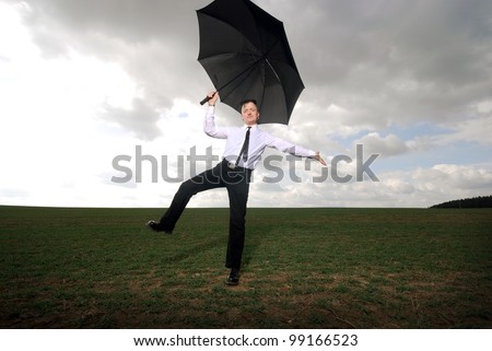 goth guy in business clothes dances with an umbrella on a meadow