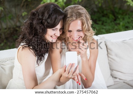 Best friends - young women sitting in summer cafe with mobile phone and having fun.