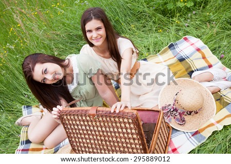 Two young women - best friends sitting on a blanket and having fun at a picnic.