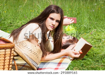 Two young women - best friends at a picnic, lying on grass and reading books.