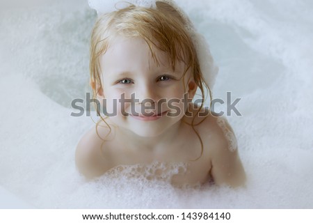 Smiling girl with a cap of foam on the head in bath