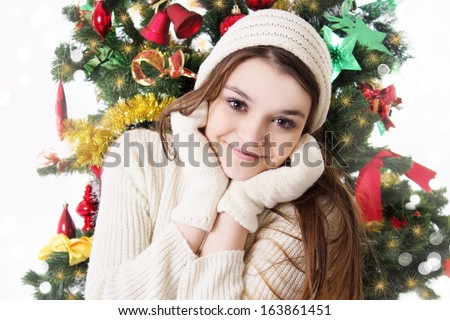 Pretty teenage girl in knitted mitten and hat under Christmas tree