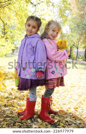 Two smiling girls standing back-to-back in autumn park