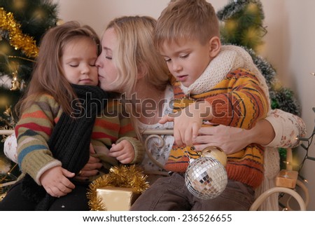 Mother kissing her two children under Christmas tree