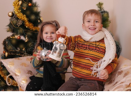 Happy sister and brother in knitted clothes having fun under golden Christmas tree