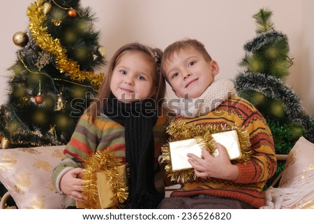 Lovely sister and brother in knitted clothes with presents under golden Christmas tree