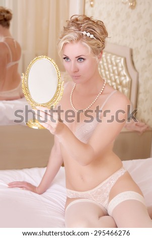 Sensual bride in lingerie and stocking looking into mirror in bedroom, focus on eyes