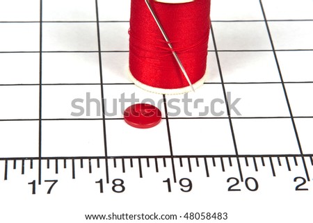 Sewing Needle with Red Thread and a Red Button on a Sewing Mat Showing Measurements