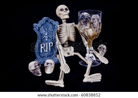 Scary Halloween skeleton with RIP headstone and glass of skeleton skulls.
