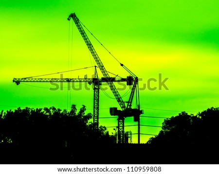 Industrial construction cranes and building silhouettes over yellow sky
