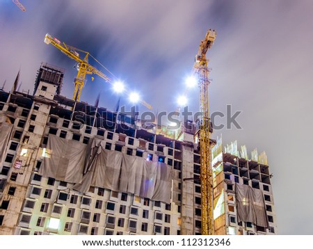 buildings under construction with cranes and illumination at dark night
