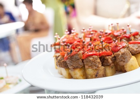 Roast meat with pineapple slices on sticks ready for wedding party or business meeting. Background of blurry party attendees walking around enjoying the meal
