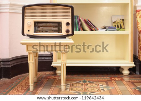 Old radio on stool with book shelf behind them