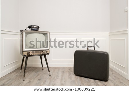 Old Television with 4 legs in the corner of vintage room and a black old telephone on it with suitcase on the right side