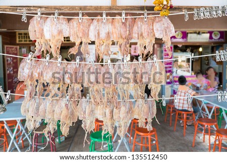 dry squid hanging on the thread with market background of family eating their meal