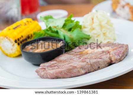 A grilled steak topped with mushrooms and dill, garden fresh corn on the cob and a steaming hot baked potato