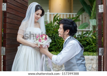 asian man on his knee giving flower to asian bride