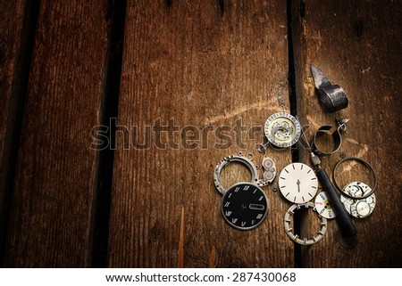 Old clock, spare parts and repair tools on a wooden background.