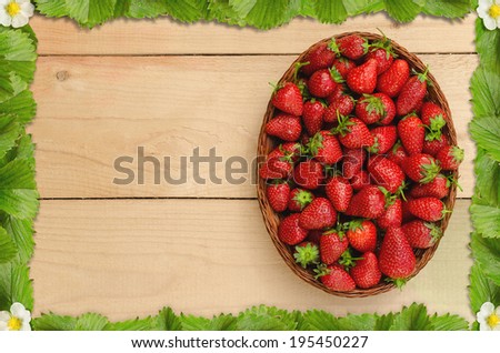 Strawberries in basket on wooden table with a frame of strawberry leaves
