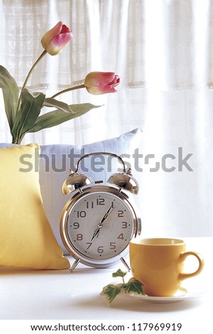 an empty cup, a metalic clock, and a vase with two tulips