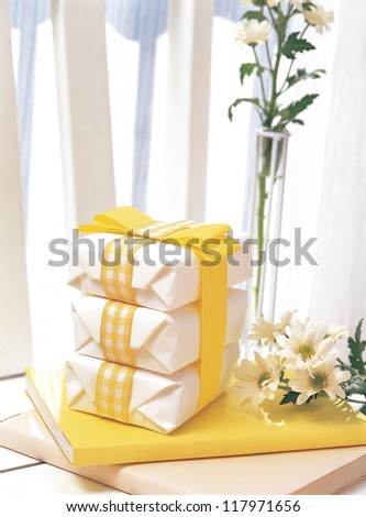 three gift boxes wrapped in a yellow ribbon placed onto a yellow book with whiter flowers by the side